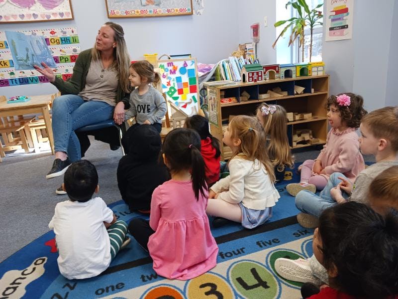Adult reading a book to a group of children sitting on a carpet in a classroom