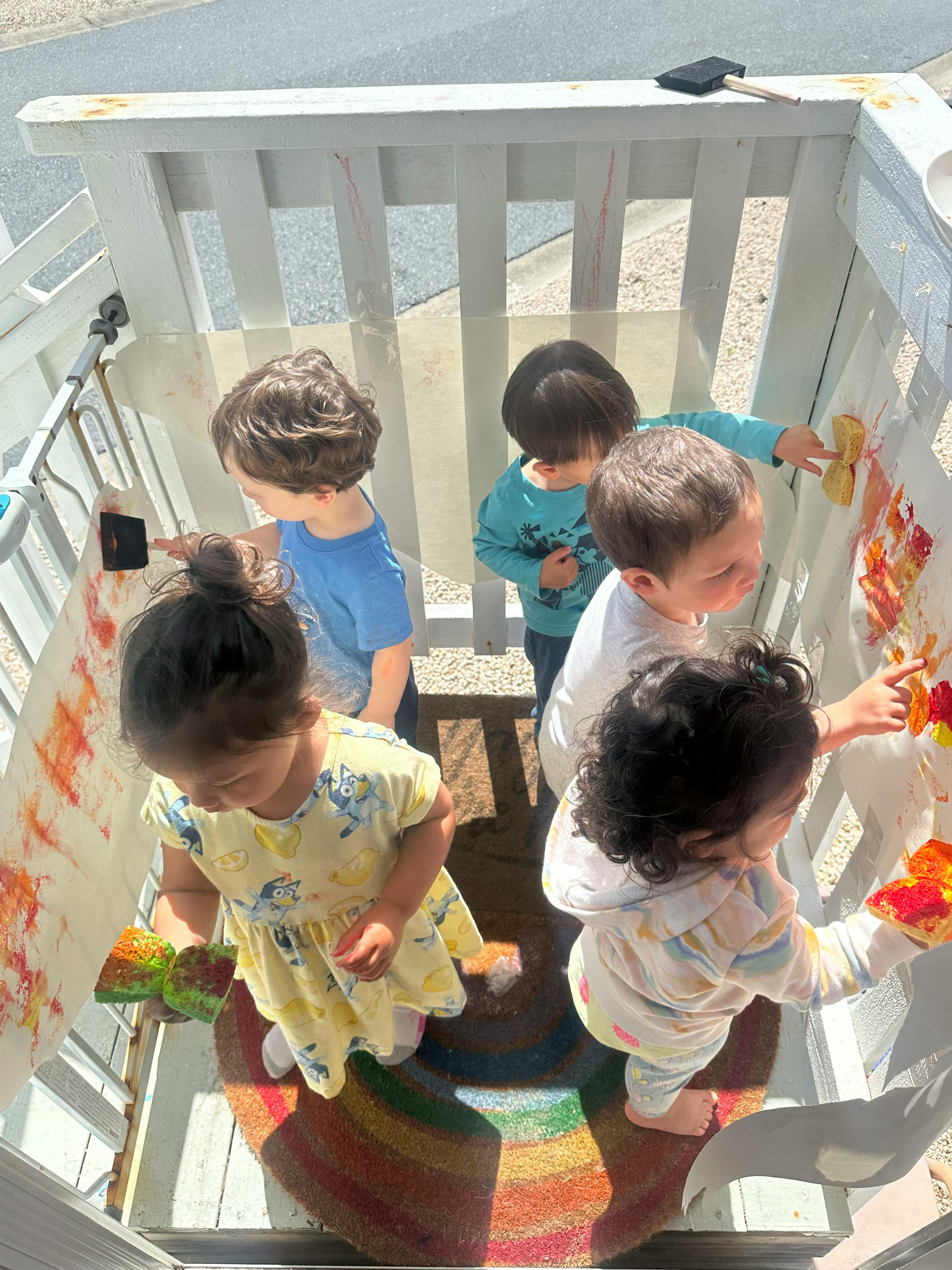 Four children painting on a white fence