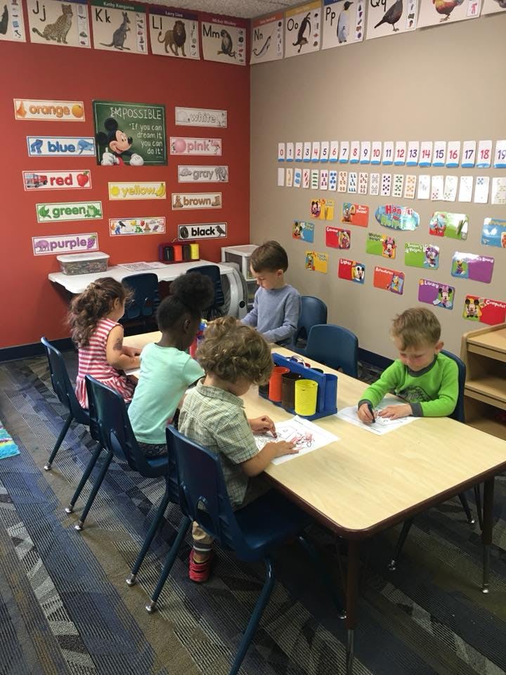 Children sitting at tables in a classroom, drawing and coloring