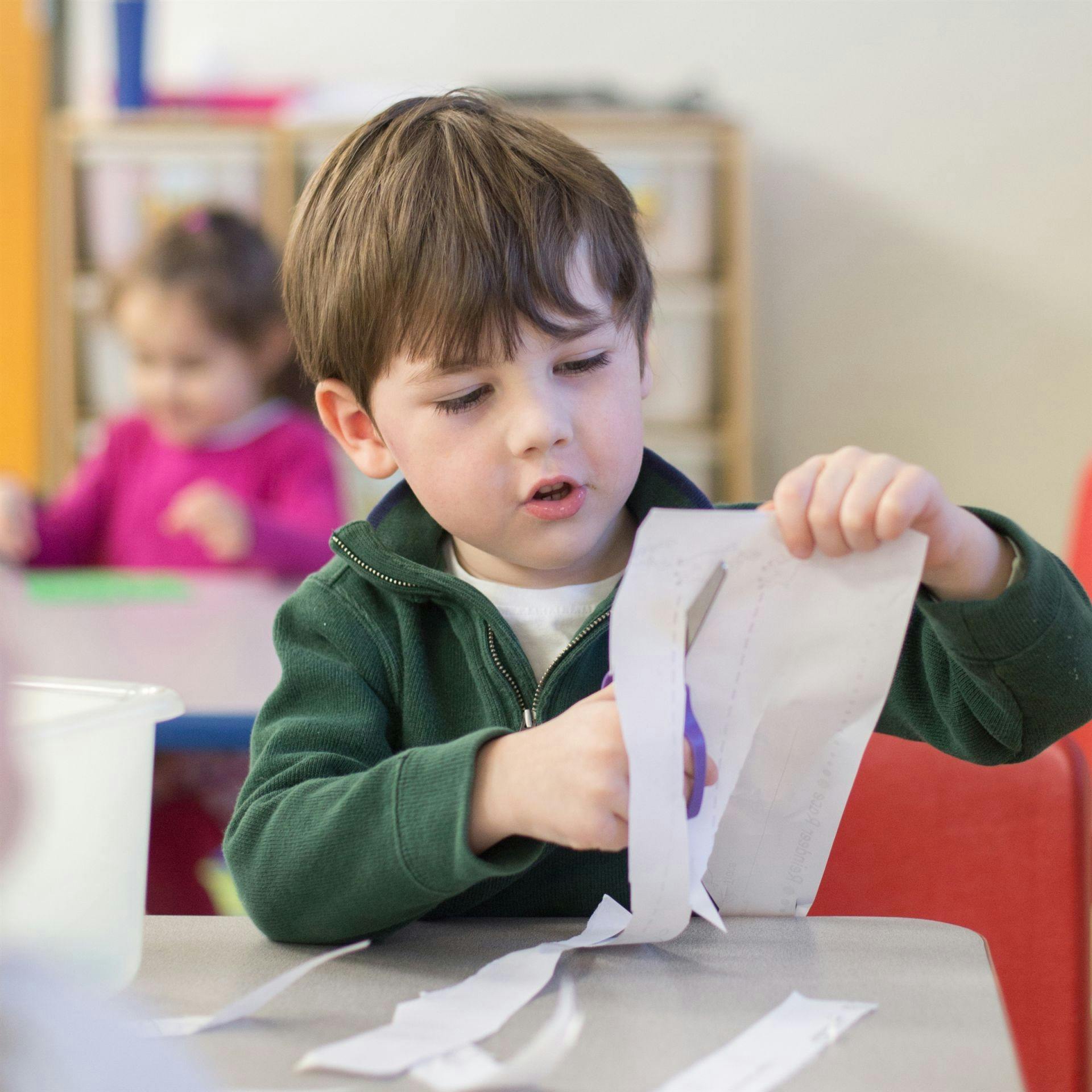 Child cutting paper with scissors in a classroom