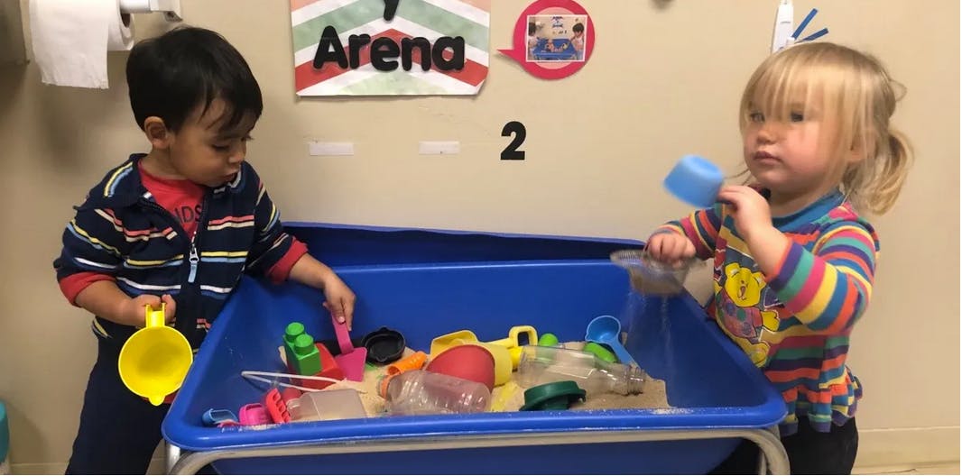 Two children playing with toys in a sand table