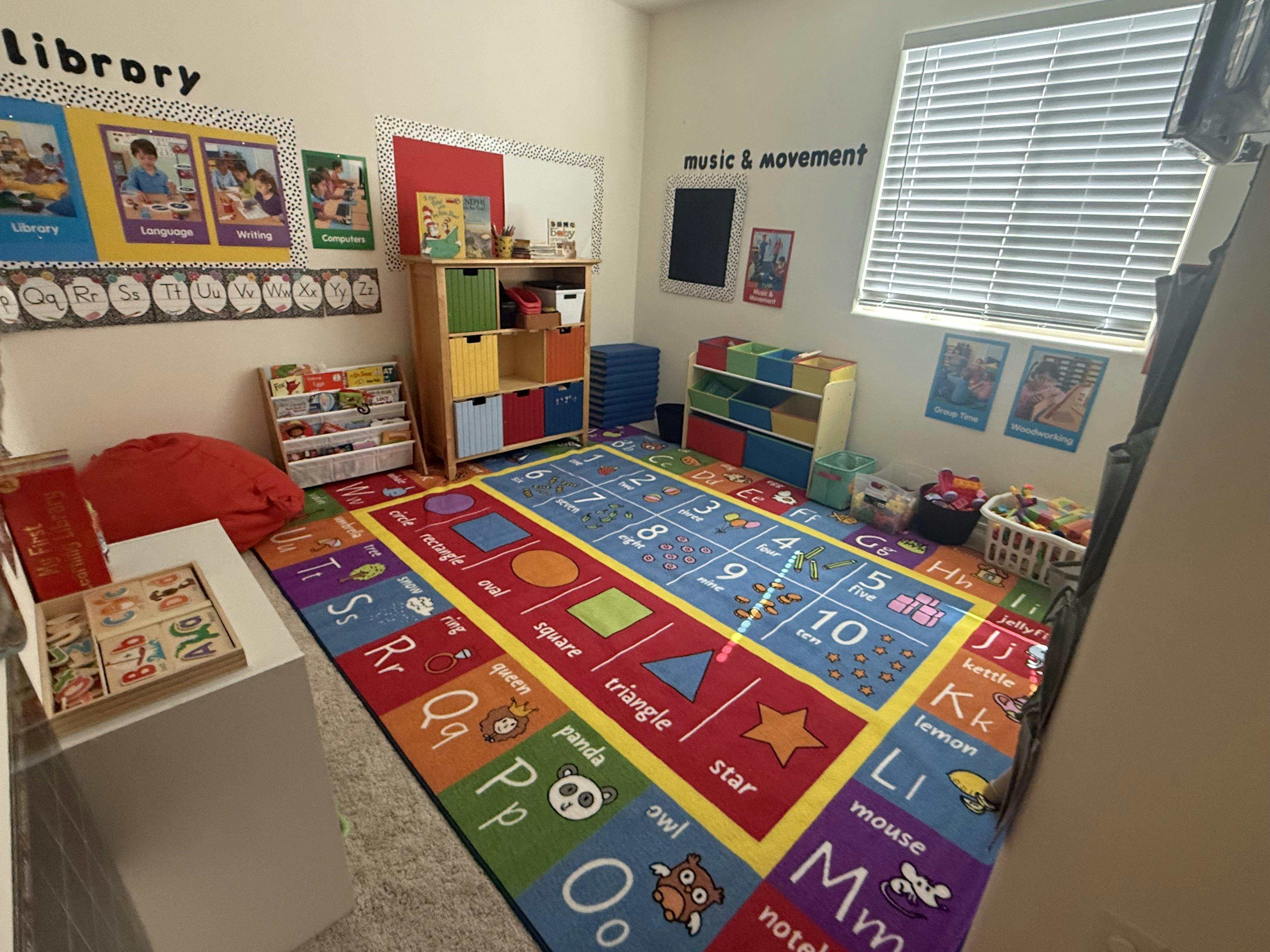 A colorful alphabet and number rug in a classroom with bookshelves and learning posters