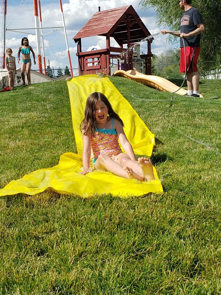 Child sitting on a yellow slip and slide on a grassy hill