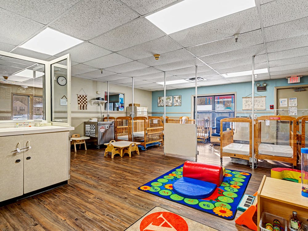 An indoor room with cribs, small tables, and play mats