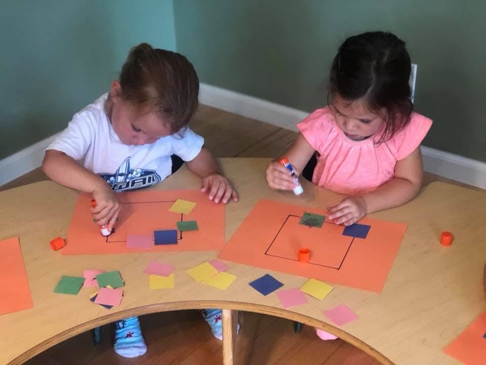 Two children gluing paper shapes onto orange paper