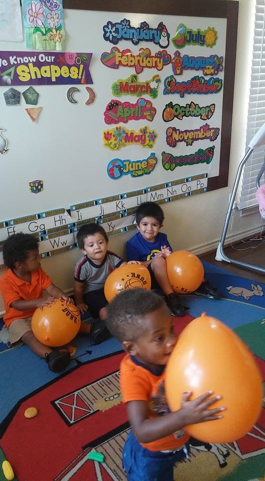 Four children playing with orange balloons in a classroom