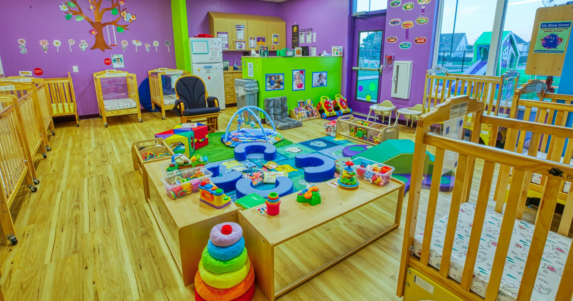 A childcare room with cribs, play mats, and toys