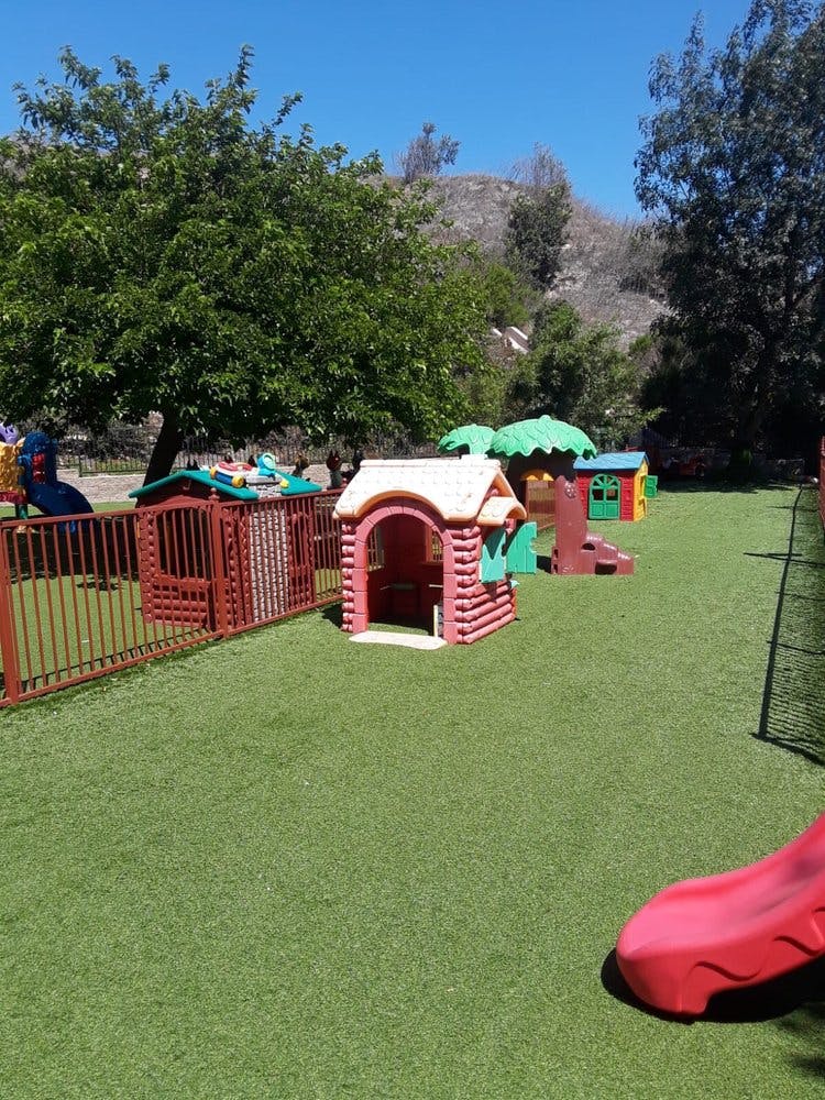 Playground with playhouses, fence, and red slide on artificial turf
