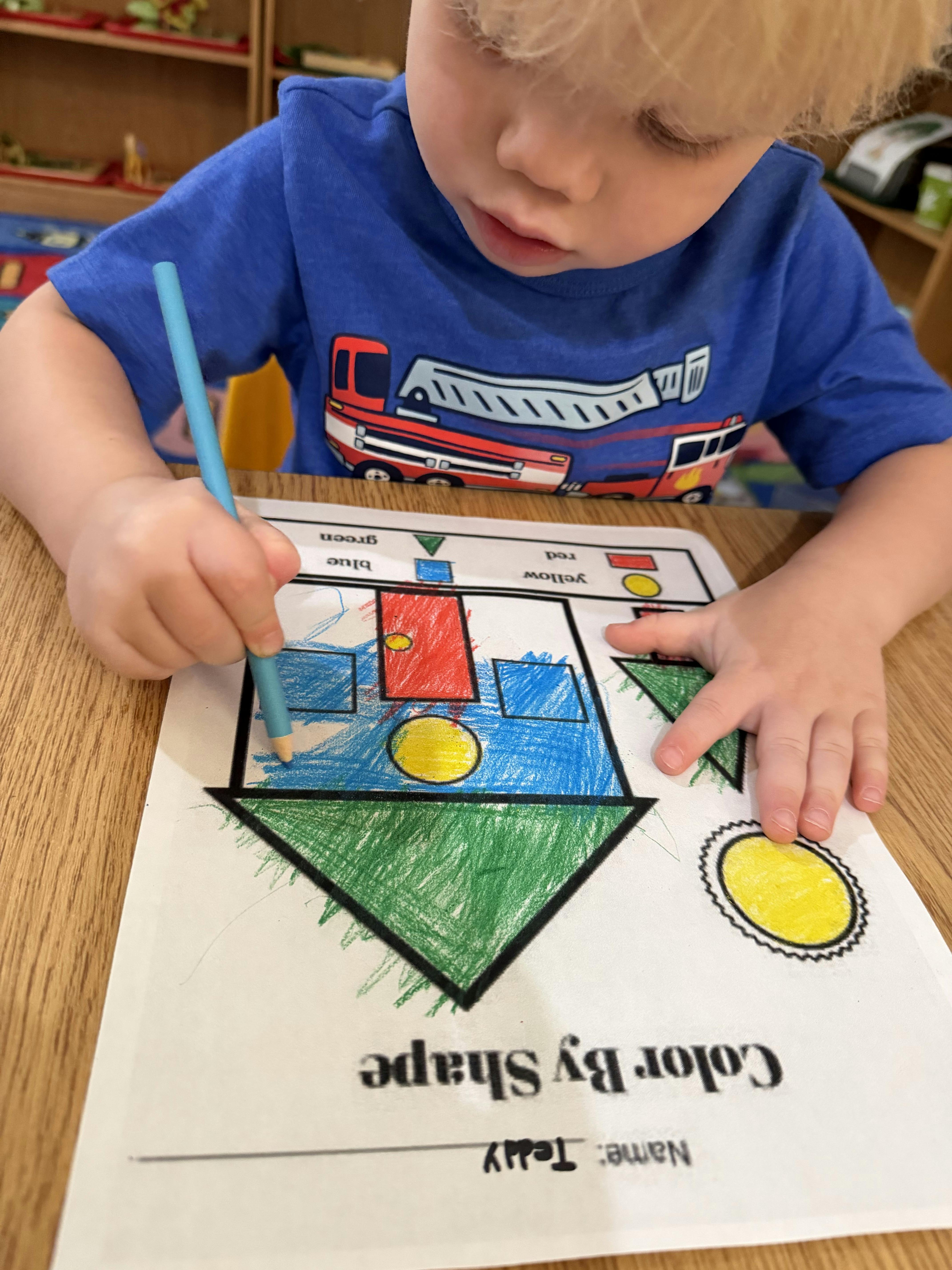 Child coloring a shape sorting worksheet with a blue crayon