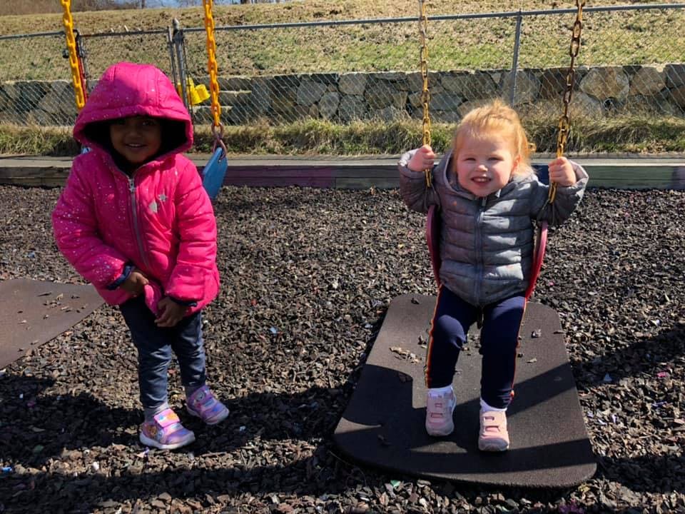 Two children on a playground, one standing and one on a swing