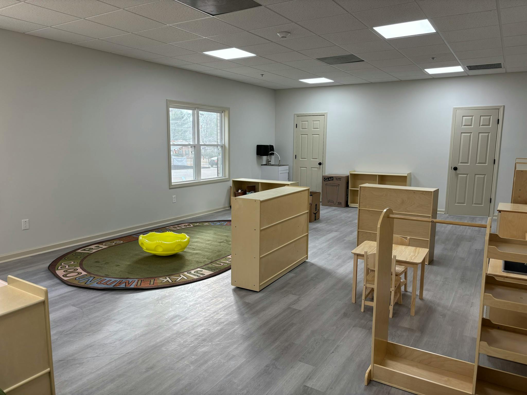 Empty classroom with small wooden furniture and a rug with letters