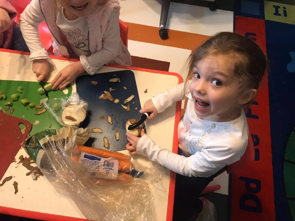 Child peeling a vegetable at a table with another child