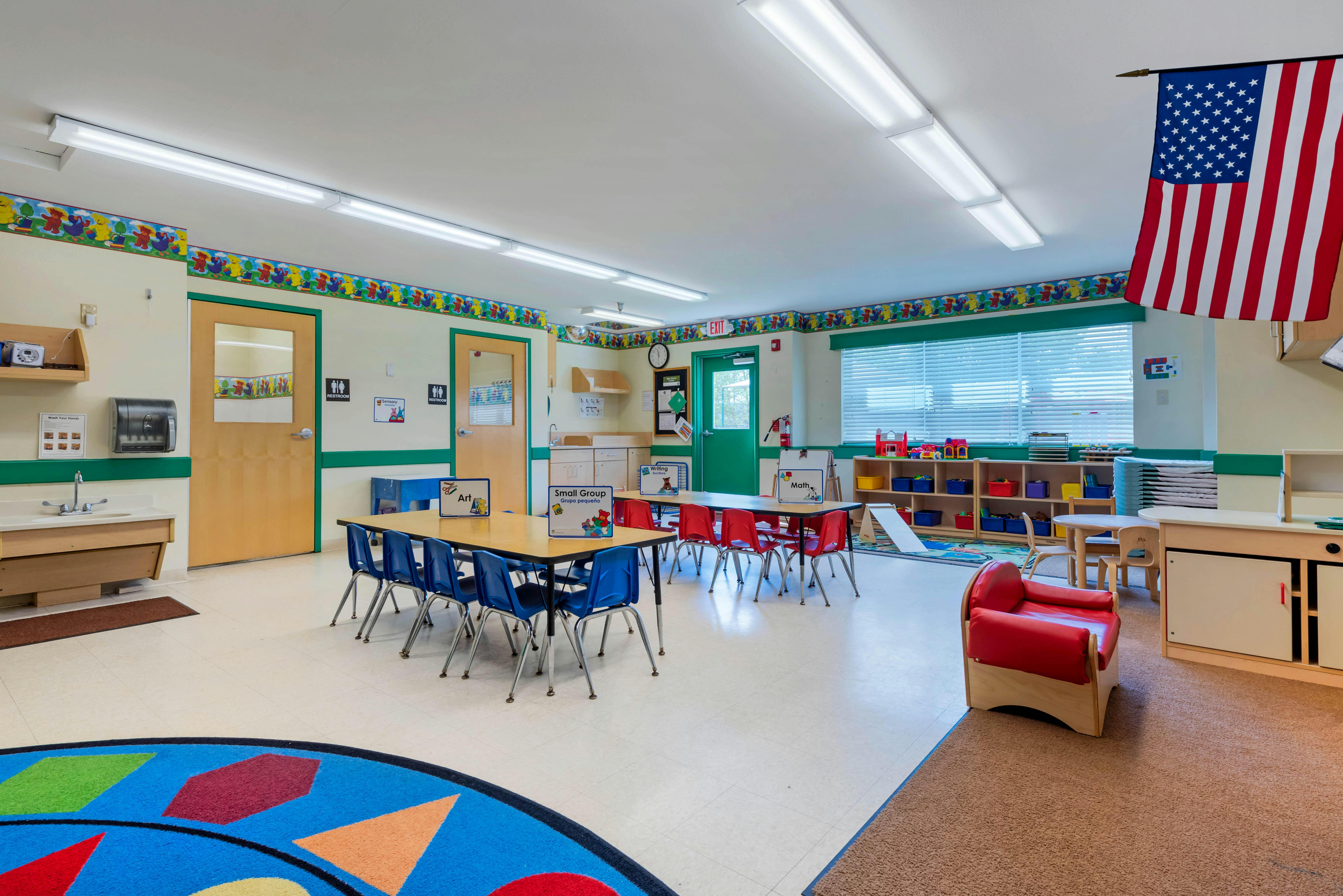 Empty classroom with small tables and chairs, and an American flag hanging