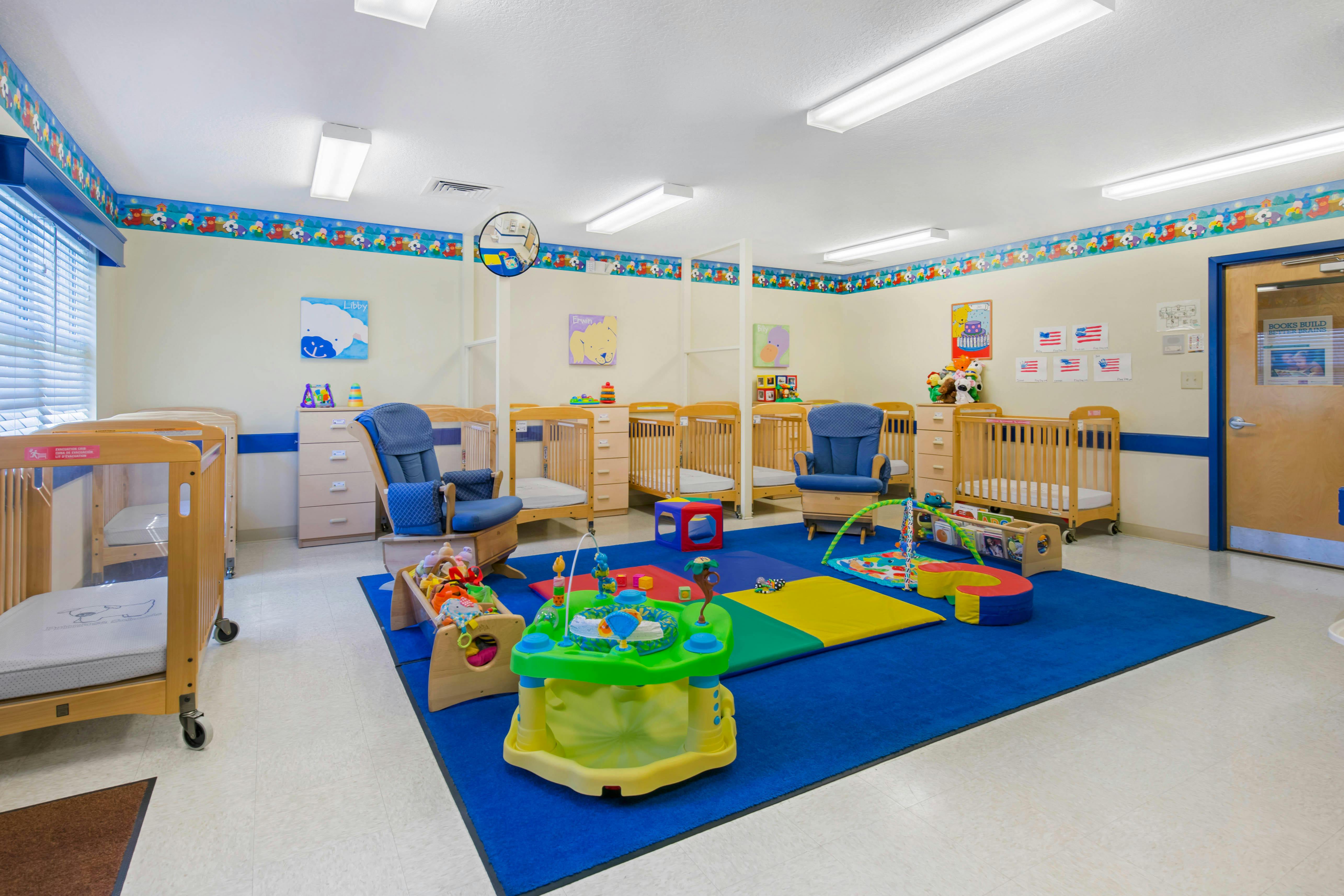 Nursery room with cribs, blue rug, and infant play equipment
