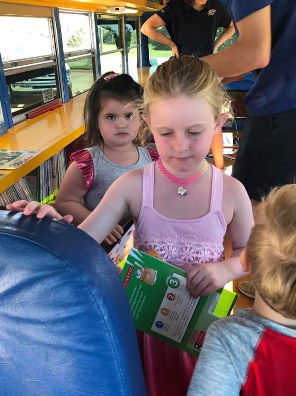 Child in pink holding a book, another child behind