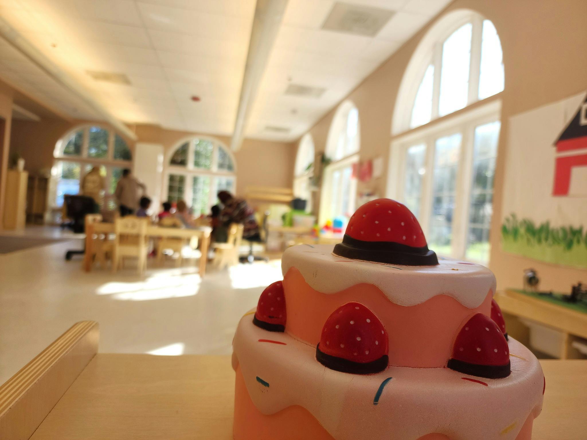 Strawberry-themed cake in foreground, people and children in background