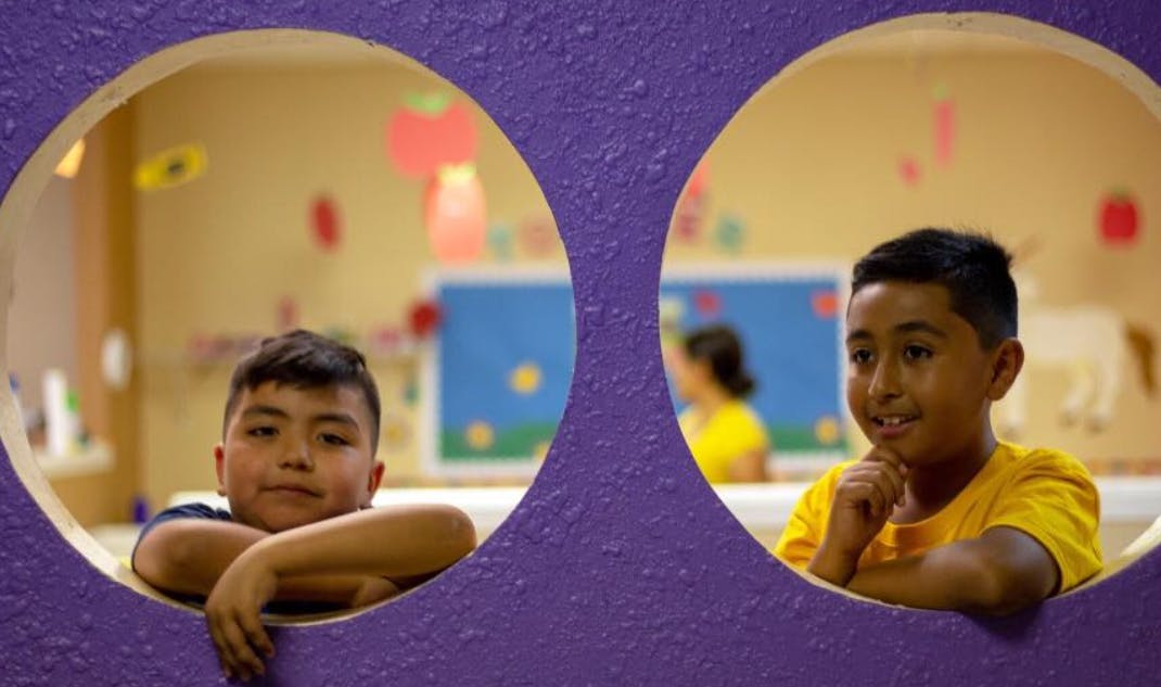 Two children looking through circular openings in a purple wall