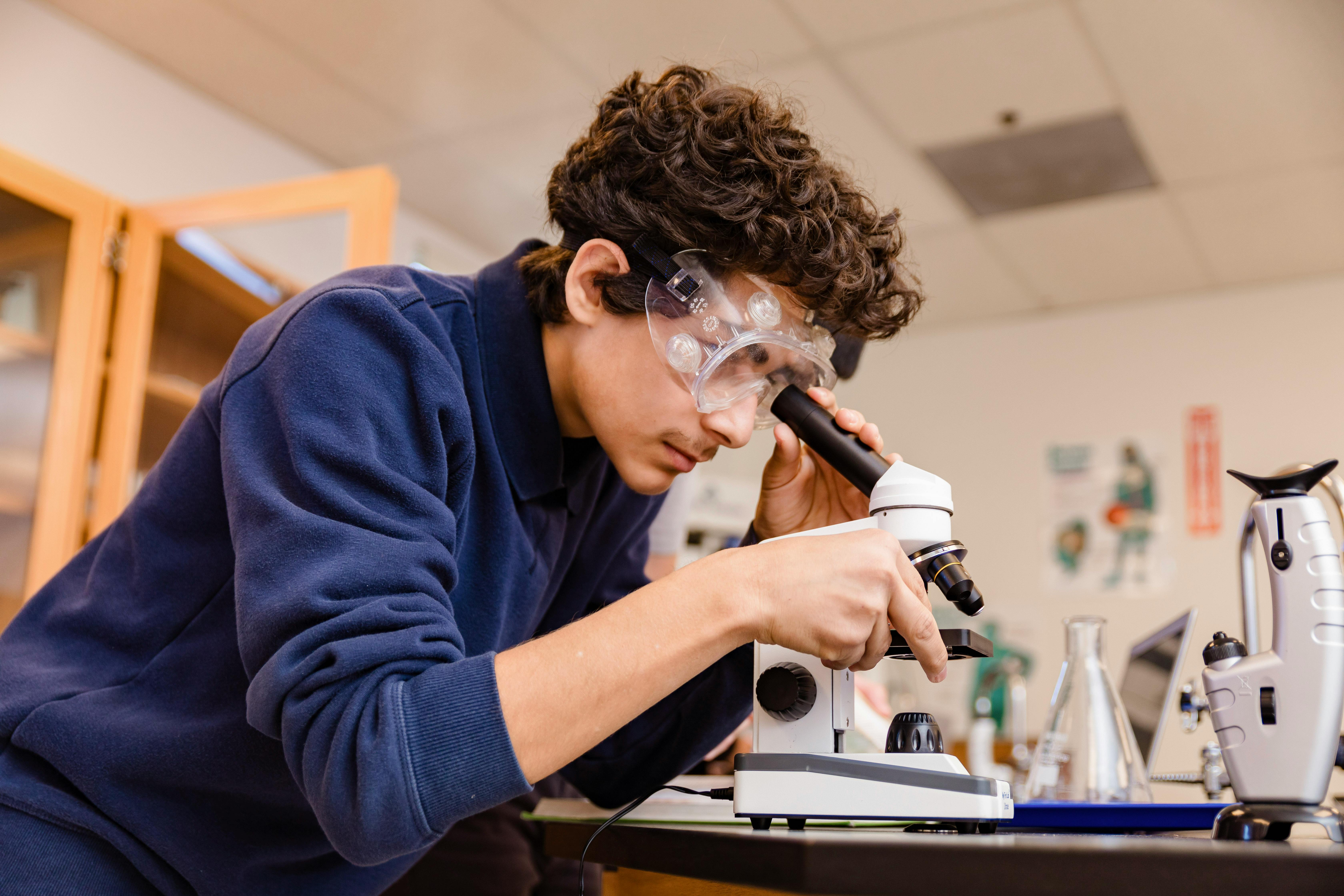 Teen wearing safety goggles looking into a microscope