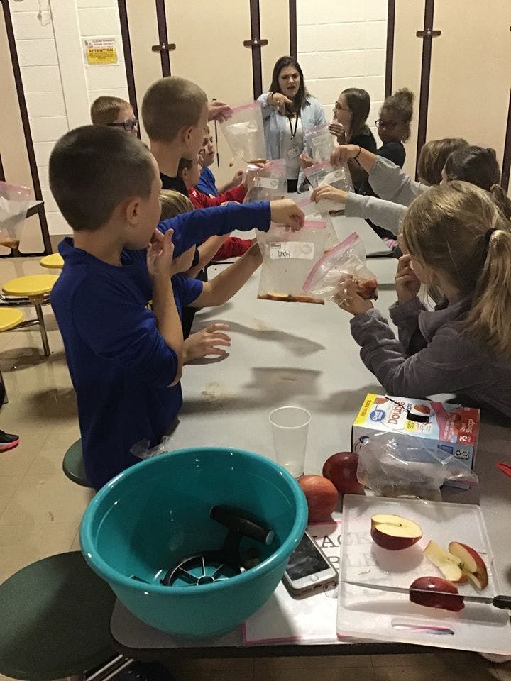 Adult and children at a table with plastic bags and apples