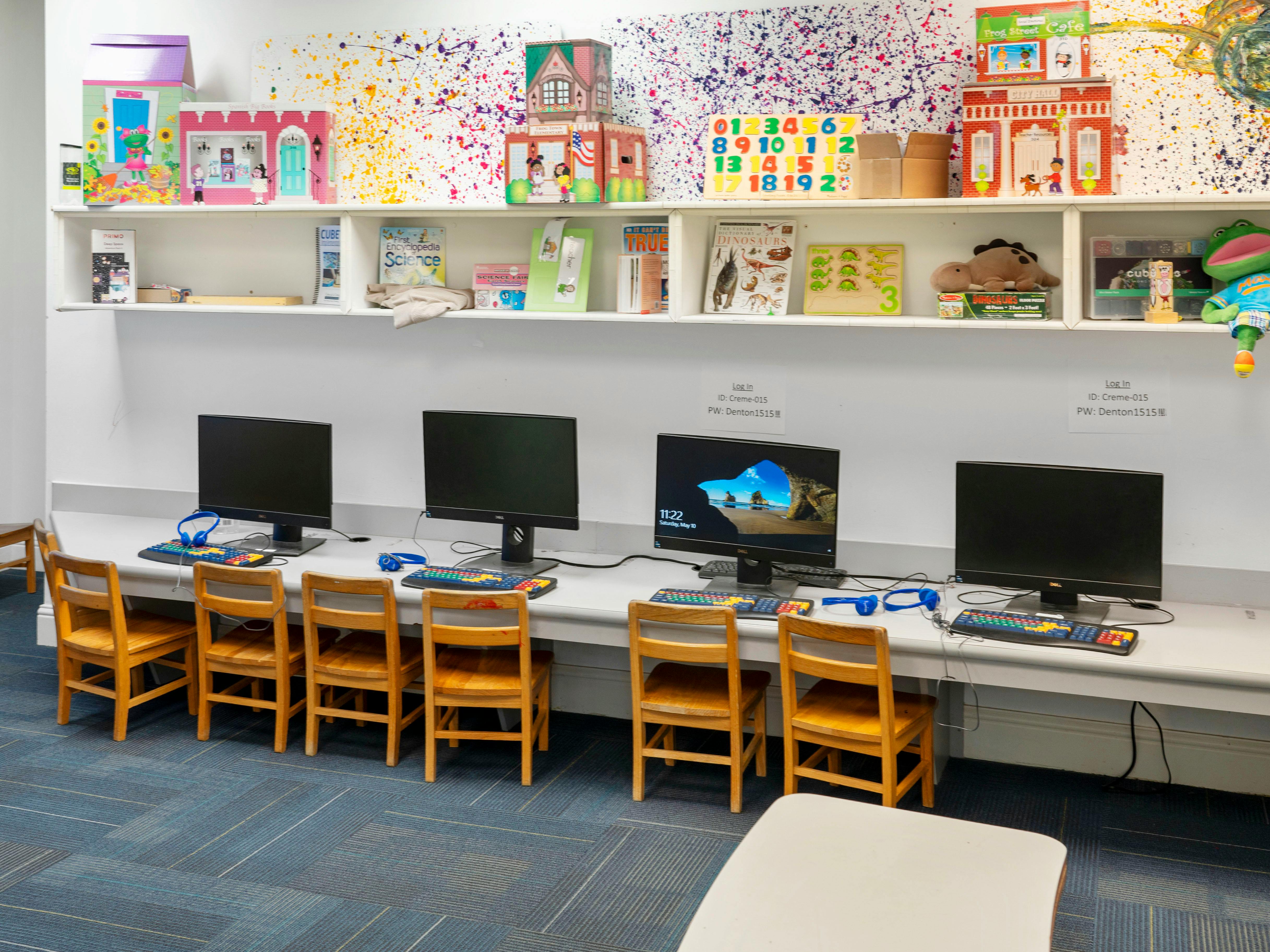 Children's computer station with multiple monitors, keyboards, headphones, and wooden chairs