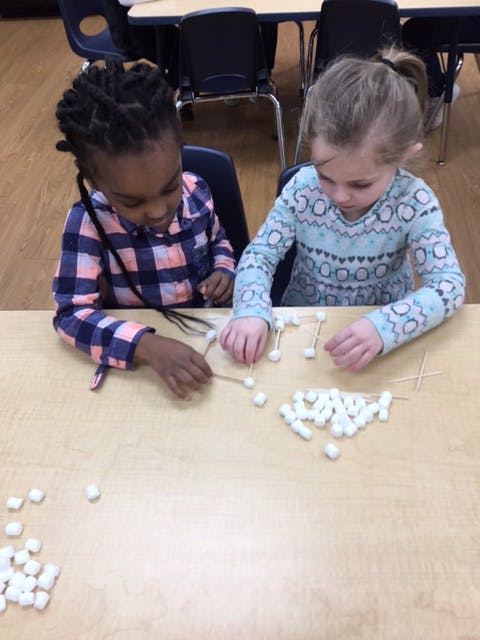 Two children building with marshmallows and toothpicks at a table