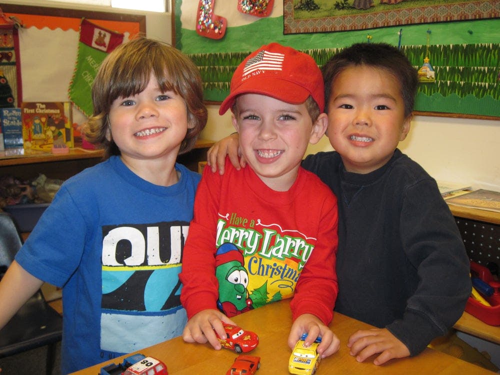 Three children smiling at a table with toy cars