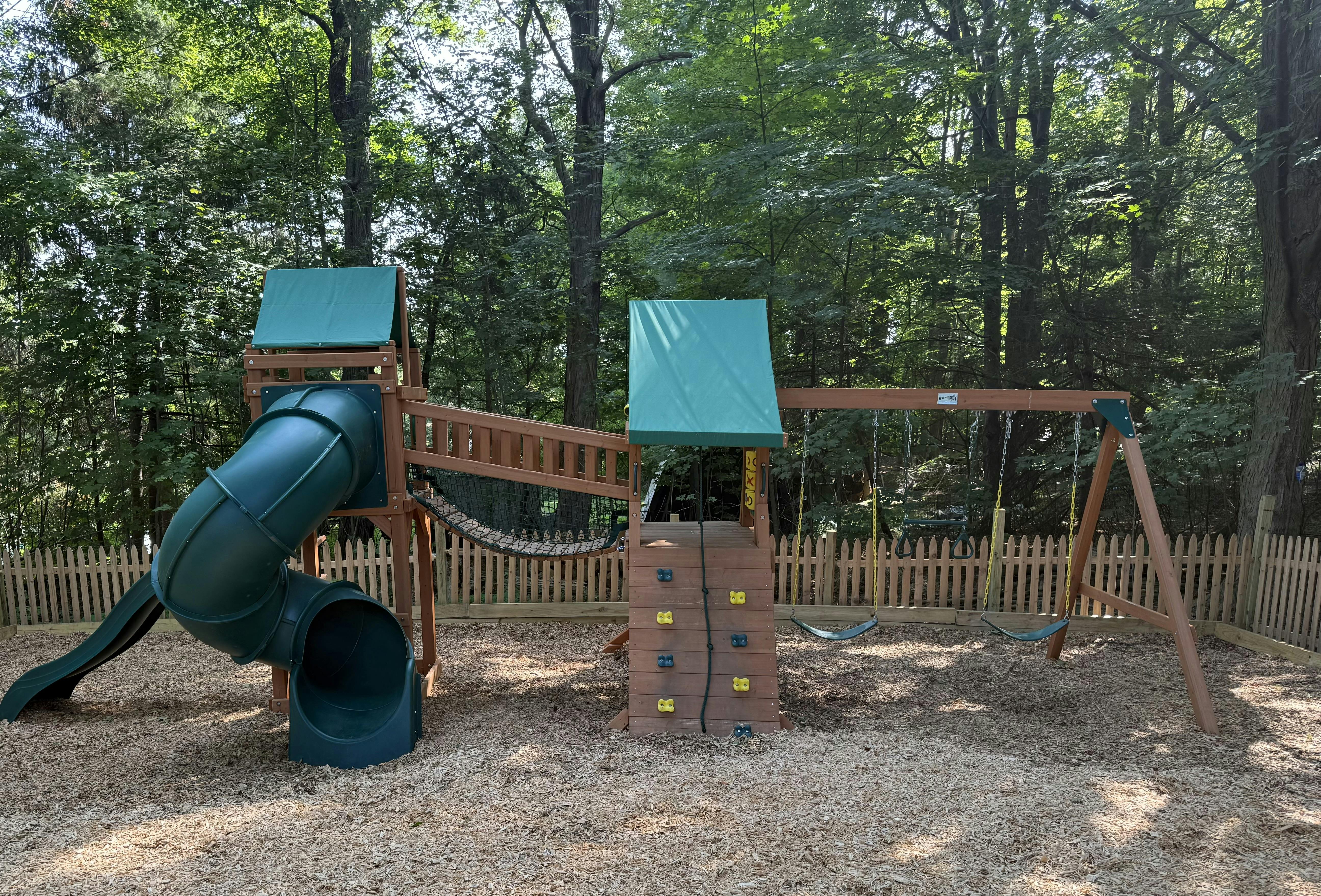 Wooden playground set with a green slide, climbing wall, and swings