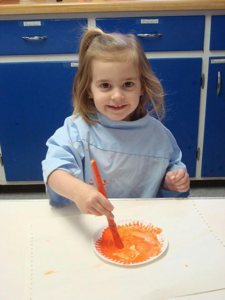 Child painting with an orange brush on a paper plate
