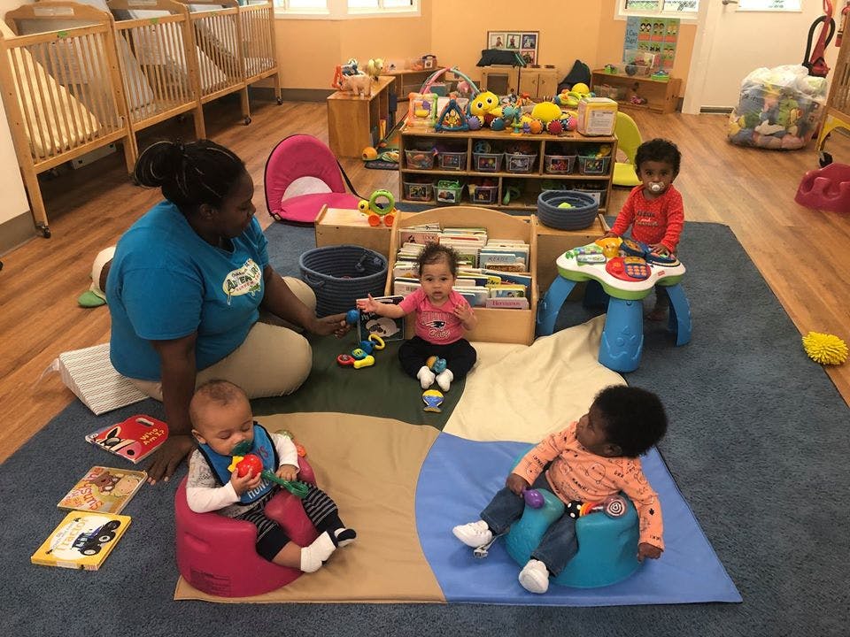 Adult and three children playing with toys on a rug