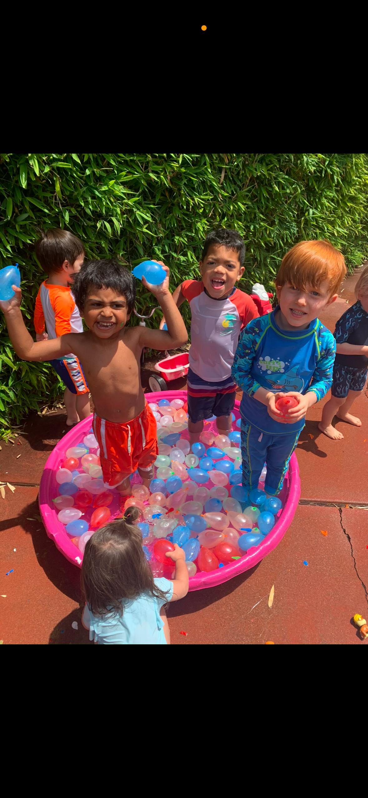 Children playing in a pink pool filled with water balloons