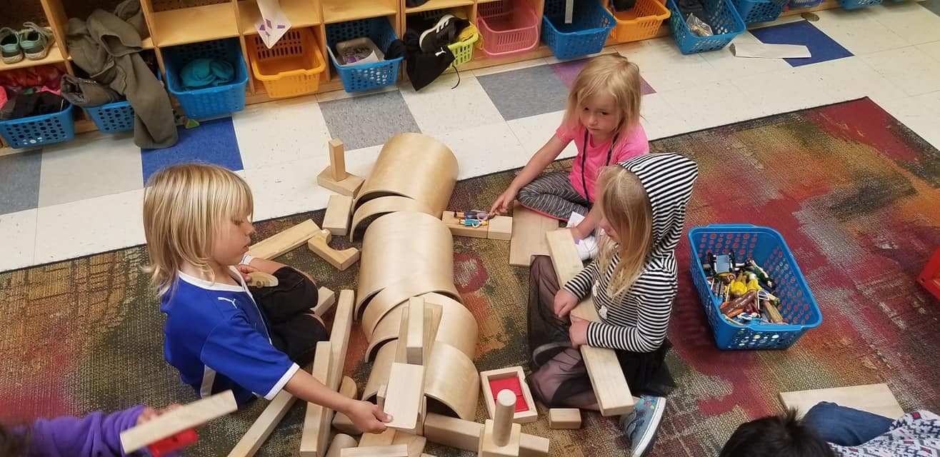 Three children playing with wooden blocks on a colorful rug