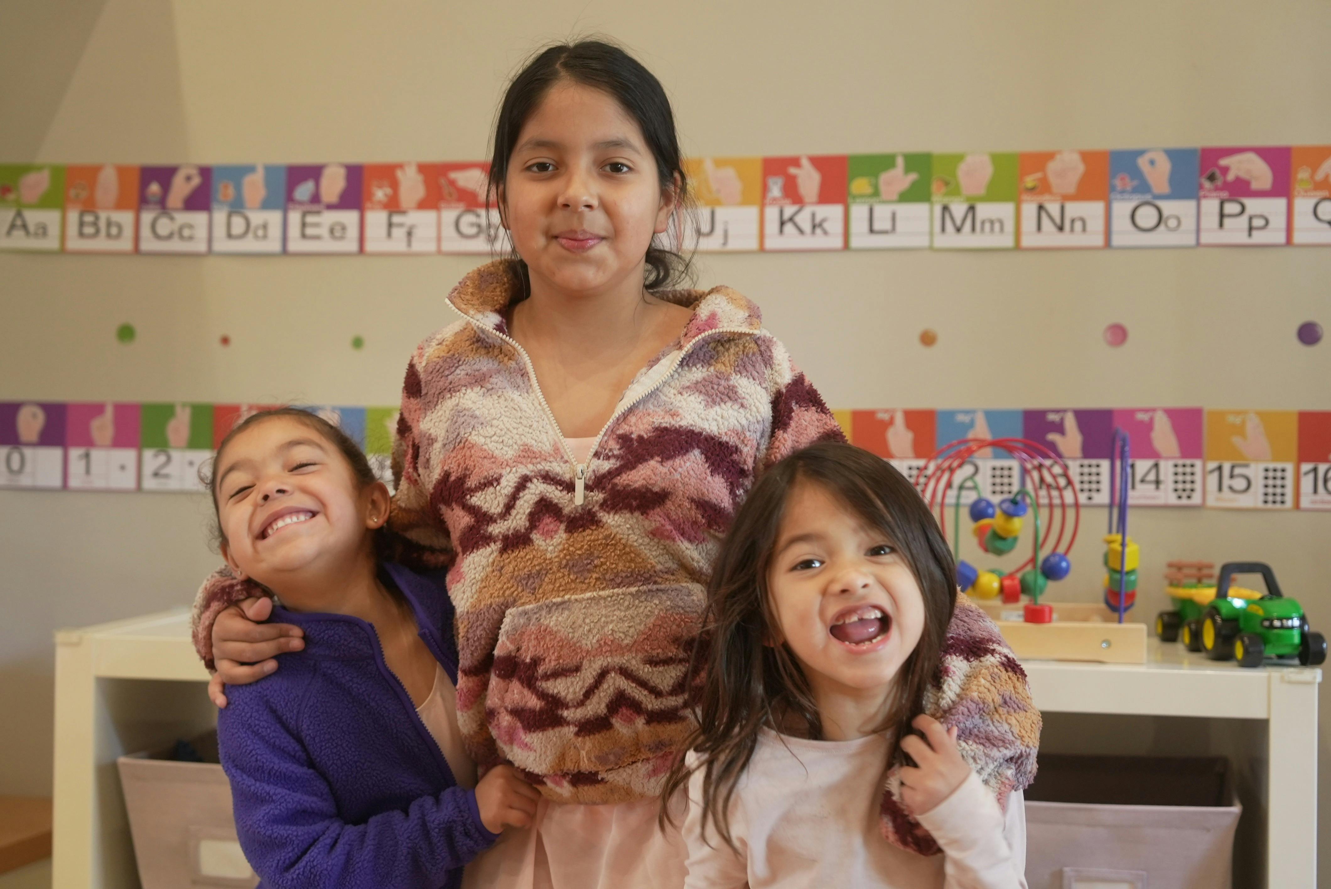 Three children smiling and posing for a photo in a classroom