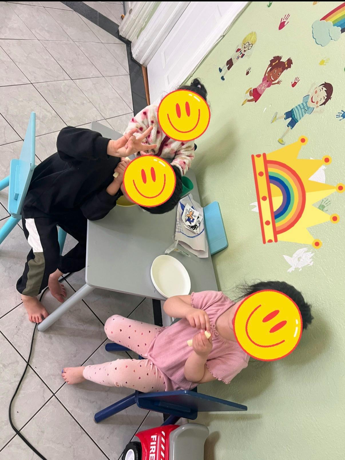 Three children sitting at a small table, one holding food