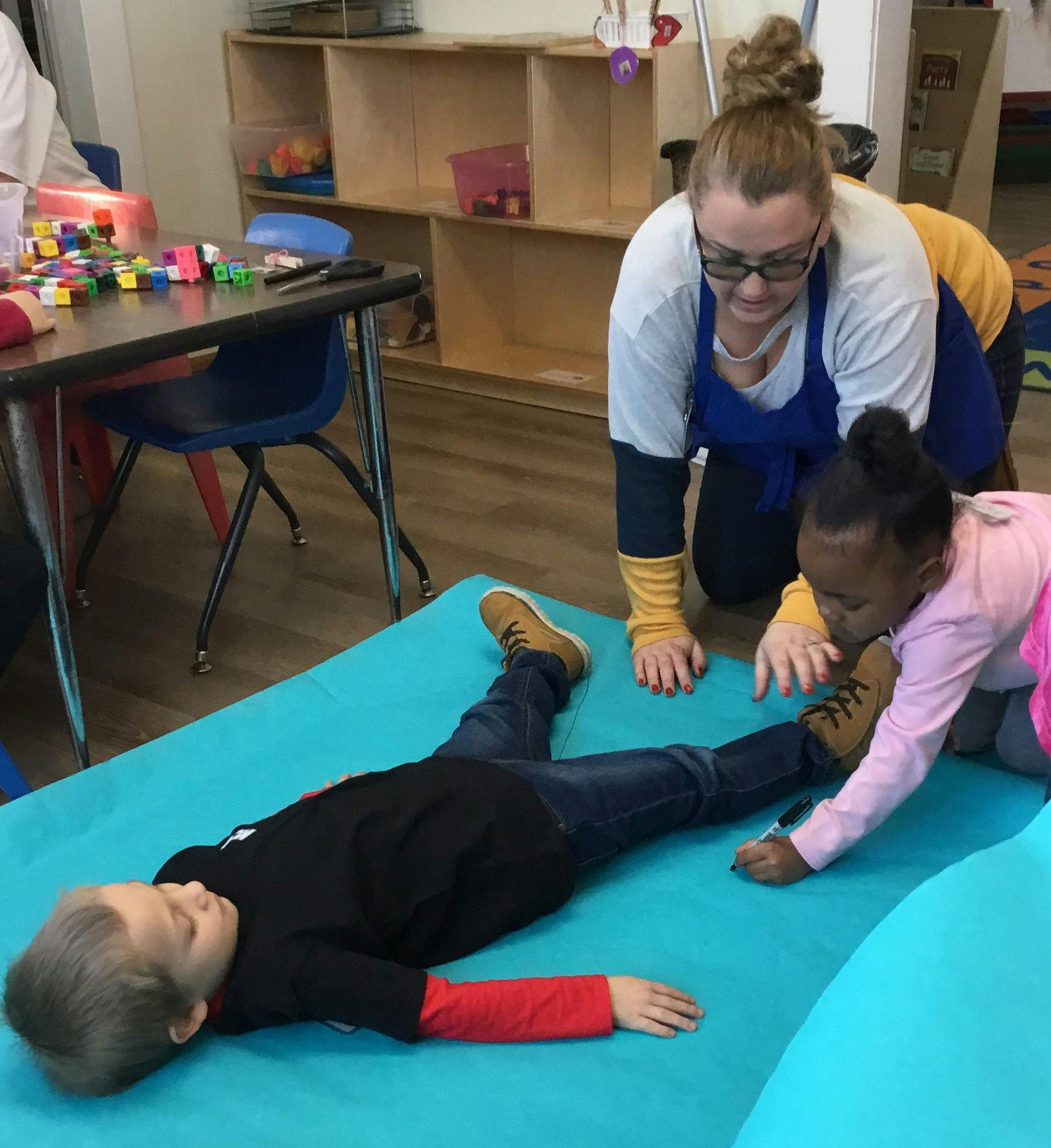 Person and child kneeling over another child lying on a mat