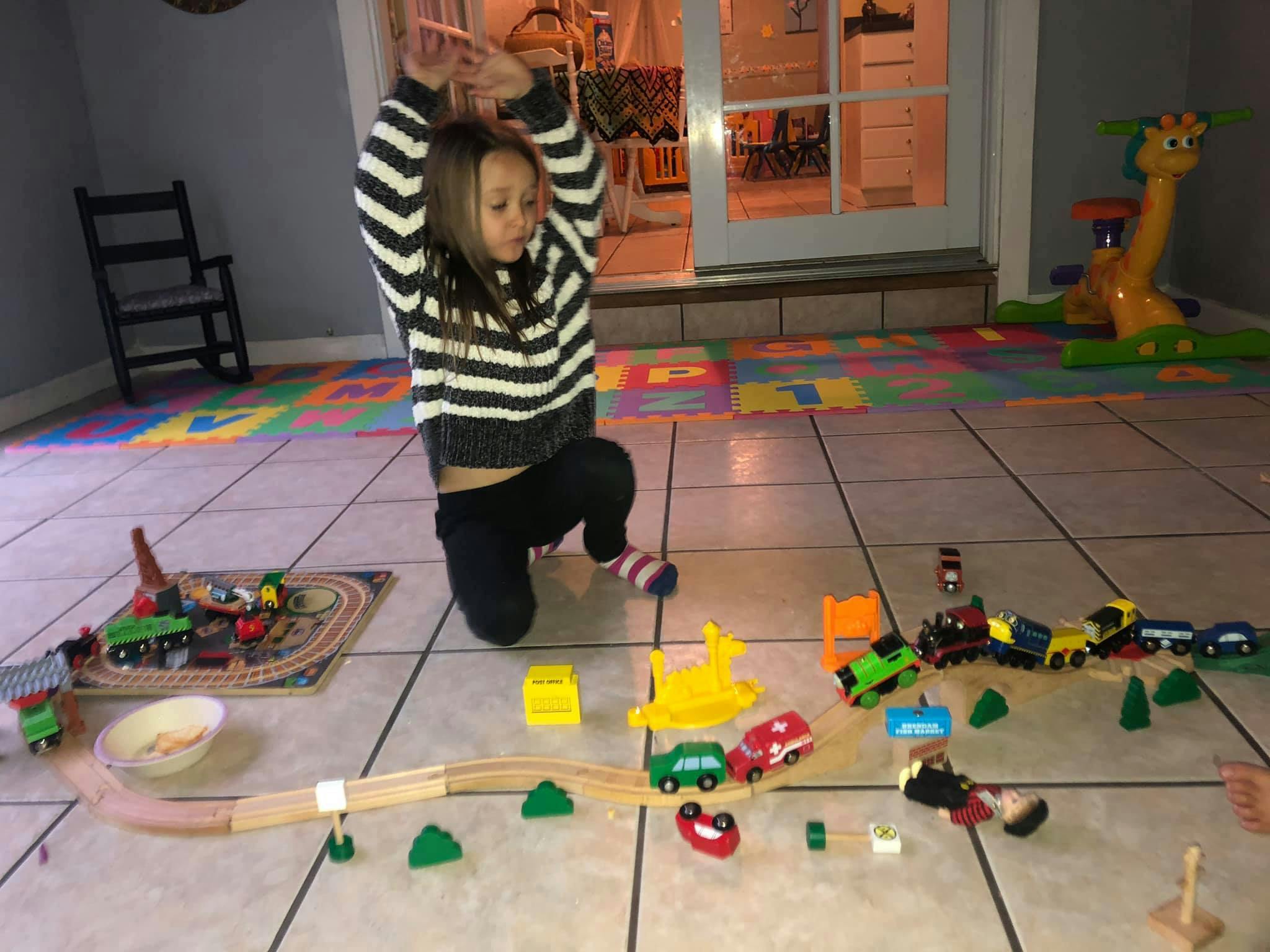 Child kneeling on floor playing with toy trains and cars