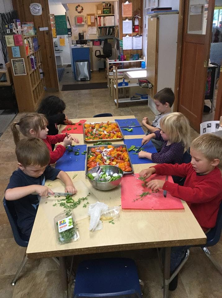 Children chopping vegetables at a table in a classroom