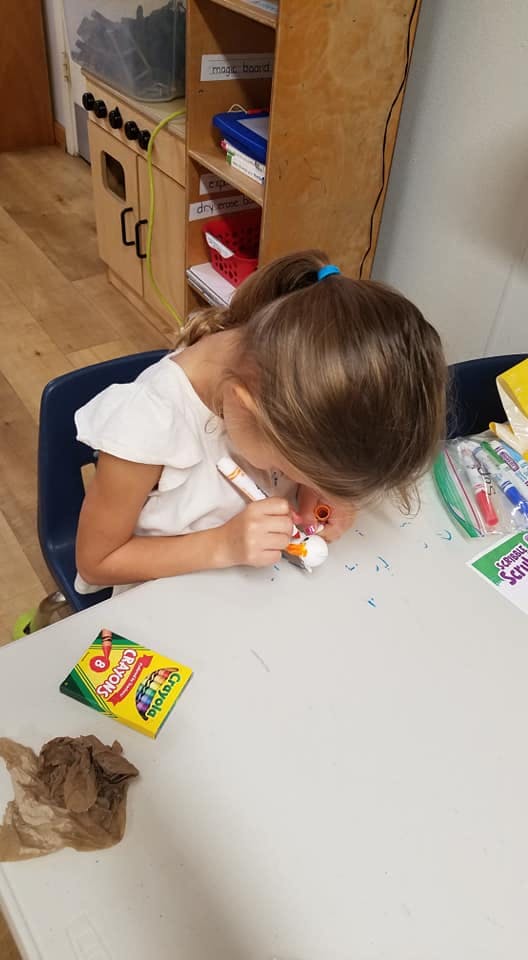 Child coloring a small object at a table