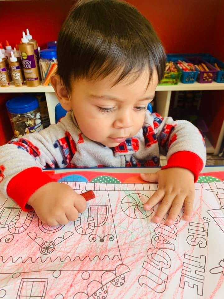 Child coloring a picture with a red crayon