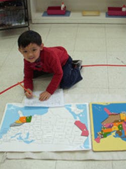 Child kneeling on floor with map puzzles
