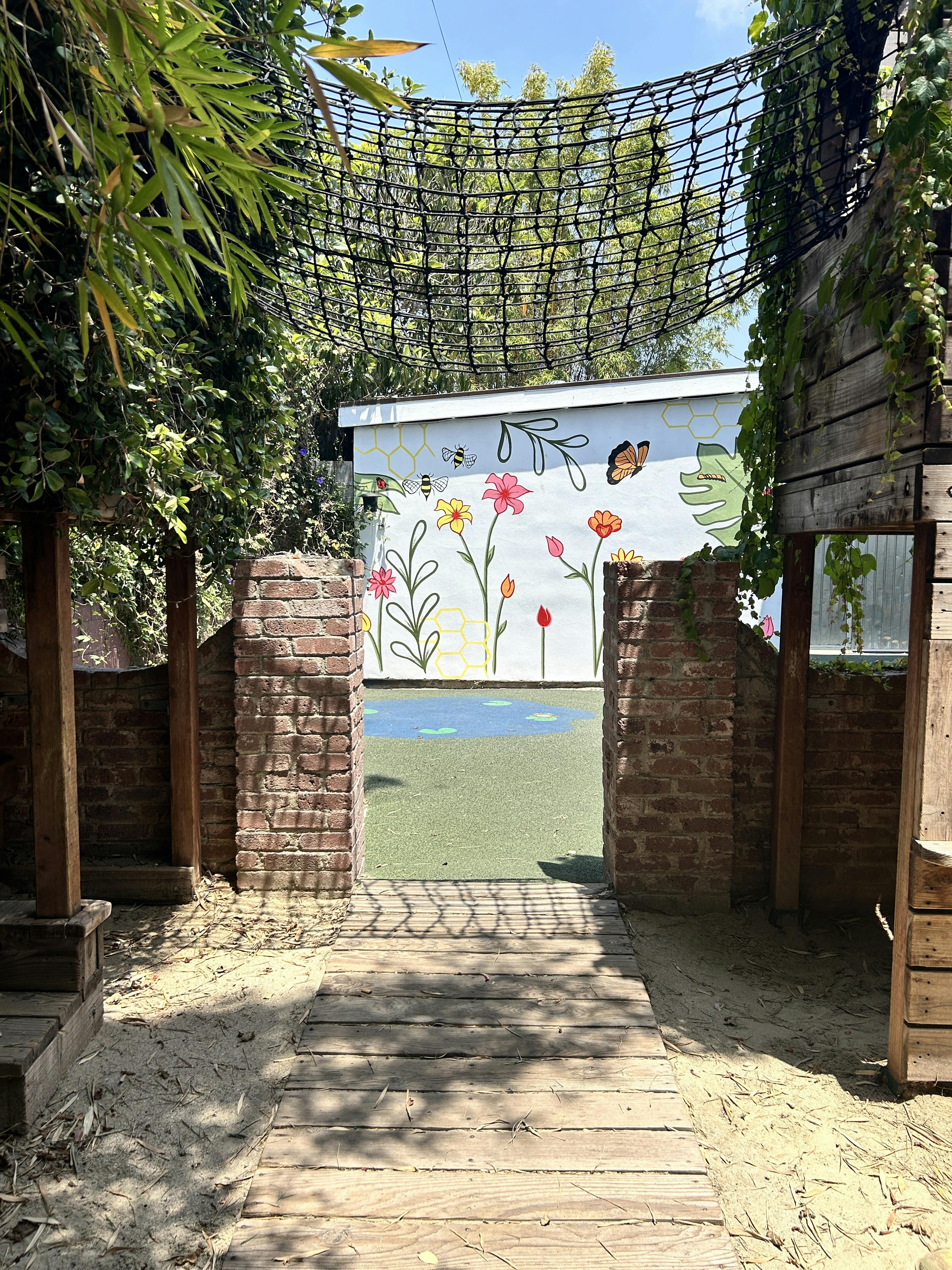 Wooden walkway through brick archway to a mural of flowers and bees on a white wall
