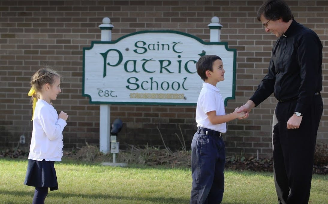 Adult and child shaking hands in front of a school sign