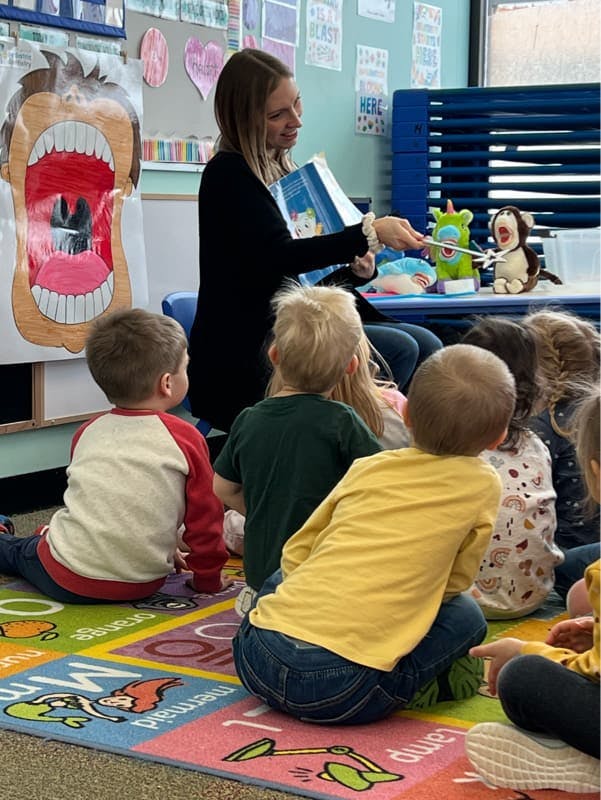 Person reading a book to children sitting on a colorful rug