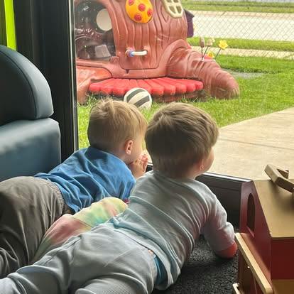 Two children lying on the floor looking out a window at a playground