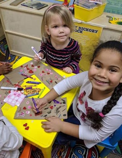 Two children drawing and coloring at a yellow table