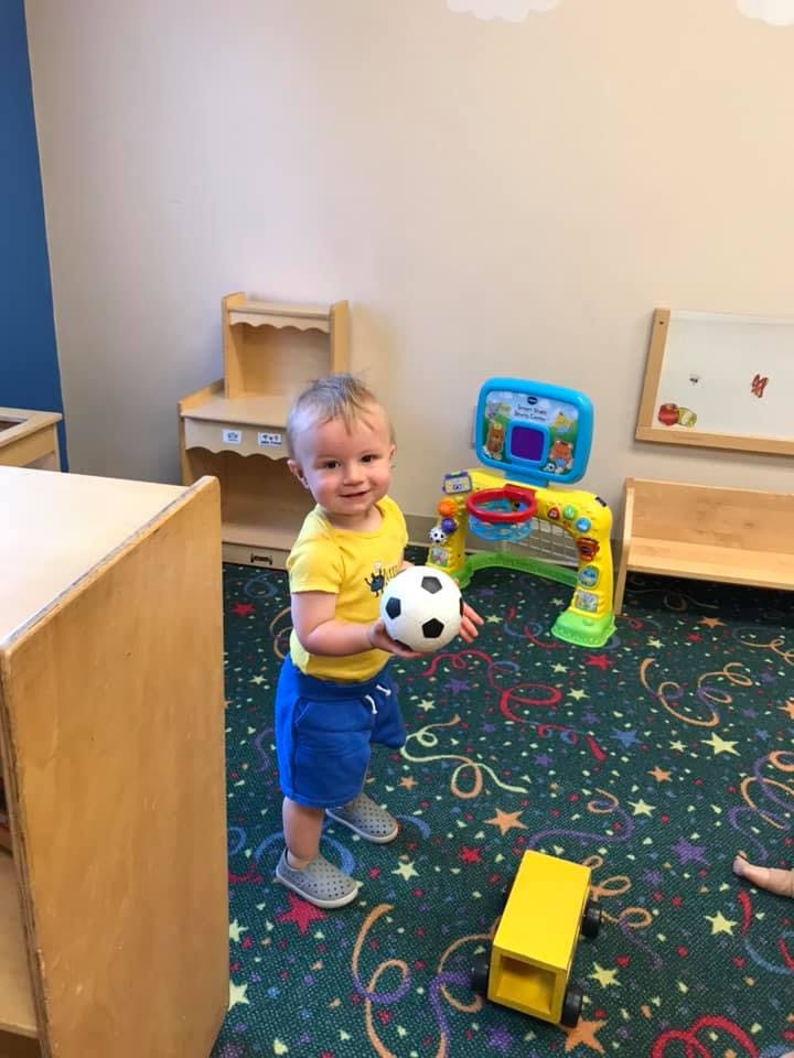 Child standing in a room holding a small soccer ball