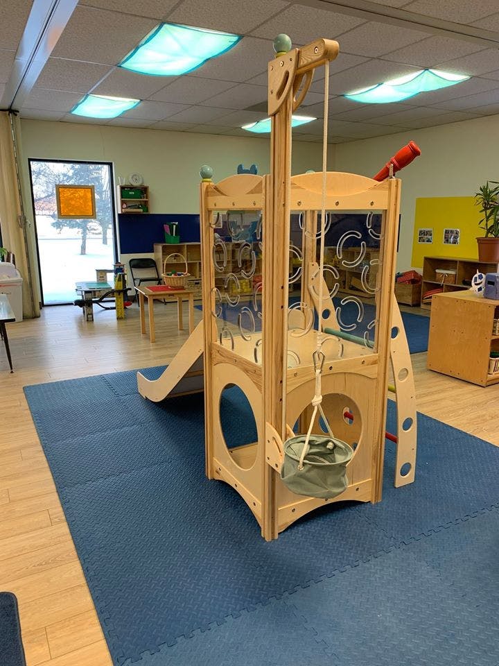 Wooden indoor play structure with a slide and bucket in a classroom
