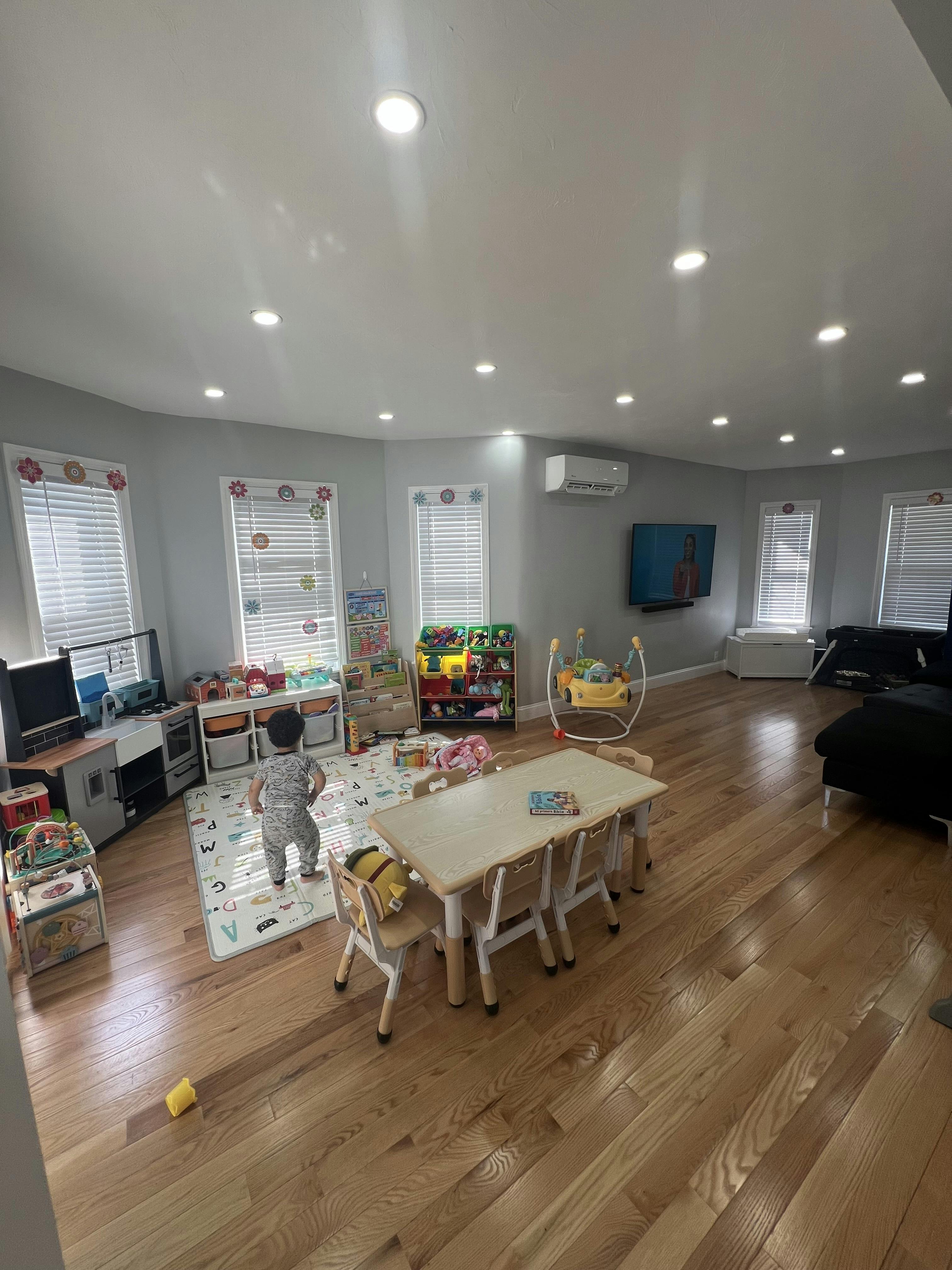 Child standing on a playmat in a room with a table and toys
