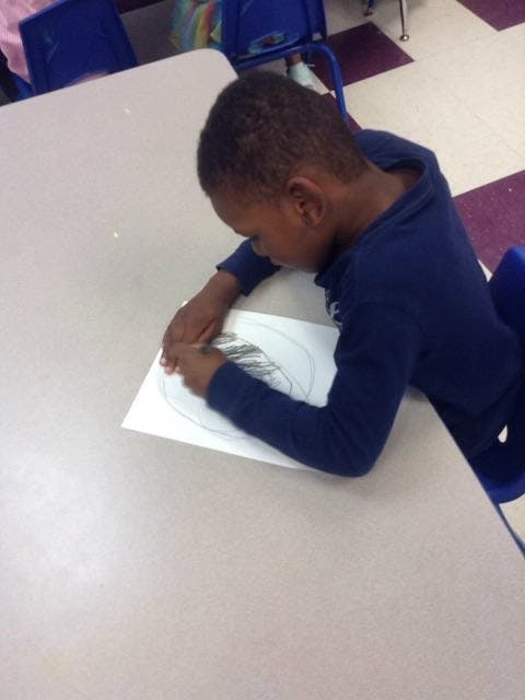 Child drawing on paper at a desk in a classroom