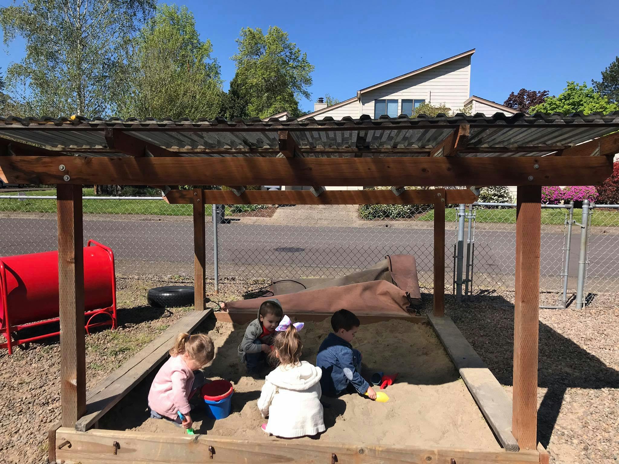 Children playing in a sandbox under a wooden shelter