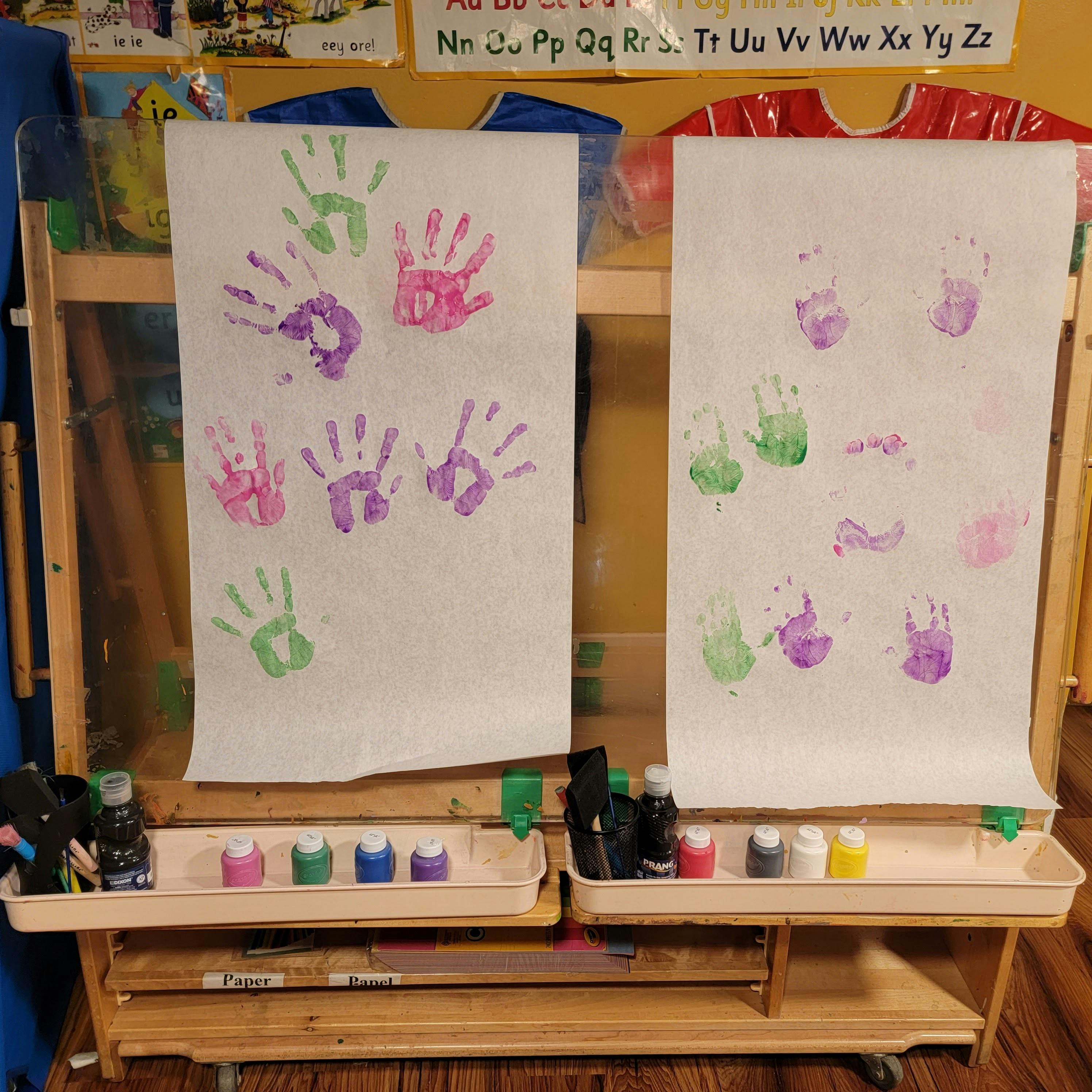 Two easels with paper showing multiple handprints in various colors
